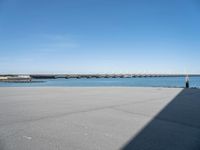 an empty beach with the sea and bridge in the back ground behind it, which are also a few small docks