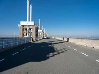 a bridge over the ocean with construction equipment in the background and two people walking on it