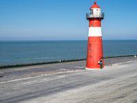 a red and white lighthouse on the beach with people walking up it to the lighthouse