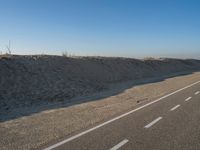 a desert road with a beach in the background and a large patch of sand on the left of the road