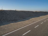 a desert road with a beach in the background and a large patch of sand on the left of the road