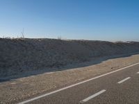 a desert road with a beach in the background and a large patch of sand on the left of the road