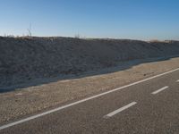 a desert road with a beach in the background and a large patch of sand on the left of the road