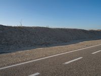 a desert road with a beach in the background and a large patch of sand on the left of the road