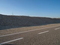 a desert road with a beach in the background and a large patch of sand on the left of the road