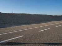 a desert road with a beach in the background and a large patch of sand on the left of the road