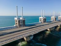 two cars driving on a large bridge over the water by sea level with wind turbines behind them