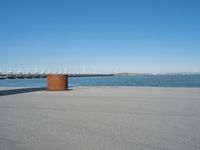 a concrete bench is standing in front of the water near a marina area with boats and buildings