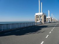 an empty highway leads along to the ocean and is lined with tall pillars and pipes