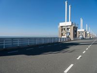 an empty highway leads along to the ocean and is lined with tall pillars and pipes