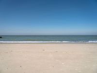 an open beach with a blue sky in the background and waves at the shore and a bright orange yellow sky