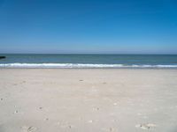 an open beach with a blue sky in the background and waves at the shore and a bright orange yellow sky