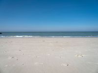 an open beach with a blue sky in the background and waves at the shore and a bright orange yellow sky