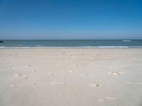 an open beach with a blue sky in the background and waves at the shore and a bright orange yellow sky