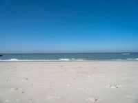 an open beach with a blue sky in the background and waves at the shore and a bright orange yellow sky