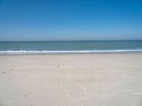 an open beach with a blue sky in the background and waves at the shore and a bright orange yellow sky