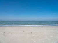 an open beach with a blue sky in the background and waves at the shore and a bright orange yellow sky