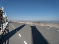 a lone shadow cast on a concrete fence near water and a street and beach behind it