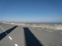 a lone shadow cast on a concrete fence near water and a street and beach behind it