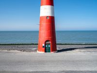 a small white and red light house stands next to a road overlooking the ocean on an open day