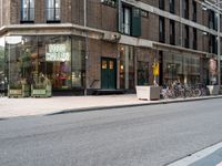 several bicycles on the street outside a restaurant in the city with buildings nearby and a bench