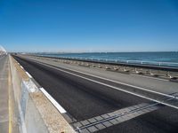 a long stretch of highway next to the ocean with two lanes divided by rails and a light rail