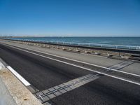 a long stretch of highway next to the ocean with two lanes divided by rails and a light rail