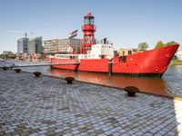 the red tugboat is docked in a harbor area at an industrial district where tall buildings are nearby