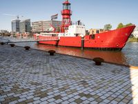 the red tugboat is docked in a harbor area at an industrial district where tall buildings are nearby