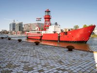 the red tugboat is docked in a harbor area at an industrial district where tall buildings are nearby