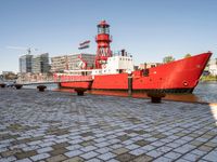 the red tugboat is docked in a harbor area at an industrial district where tall buildings are nearby