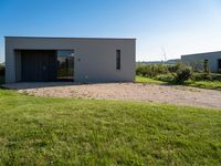 a house with a concrete driveway is surrounded by grass and graveled ground under blue sky