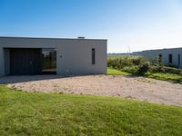 a house with a concrete driveway is surrounded by grass and graveled ground under blue sky