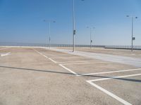 empty parking lot with poles, lights and parking meters on the ground behind it is a bridge