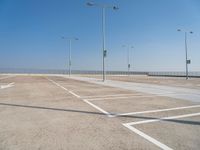 empty parking lot with poles, lights and parking meters on the ground behind it is a bridge