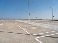 empty parking lot with poles, lights and parking meters on the ground behind it is a bridge