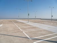 empty parking lot with poles, lights and parking meters on the ground behind it is a bridge