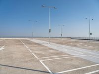 empty parking lot with poles, lights and parking meters on the ground behind it is a bridge