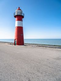 the lighthouse is red and white with a blue sky in the background from a low perspective