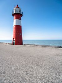 the lighthouse is red and white with a blue sky in the background from a low perspective