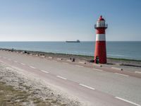 the lighthouse is by the water with boats out on the shore and people walking near the shore