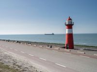 the lighthouse is by the water with boats out on the shore and people walking near the shore