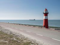 the lighthouse is by the water with boats out on the shore and people walking near the shore