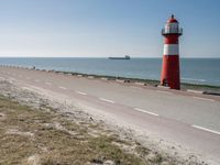 the lighthouse is by the water with boats out on the shore and people walking near the shore