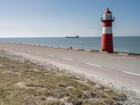 the lighthouse is by the water with boats out on the shore and people walking near the shore