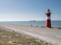 the lighthouse is by the water with boats out on the shore and people walking near the shore