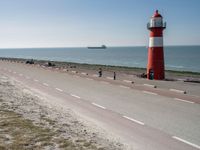 the lighthouse is by the water with boats out on the shore and people walking near the shore