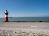 a red and white lighthouse with blue sky near a road and car on it's side