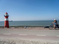 a red and white lighthouse with blue sky near a road and car on it's side