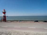 a red and white lighthouse with blue sky near a road and car on it's side